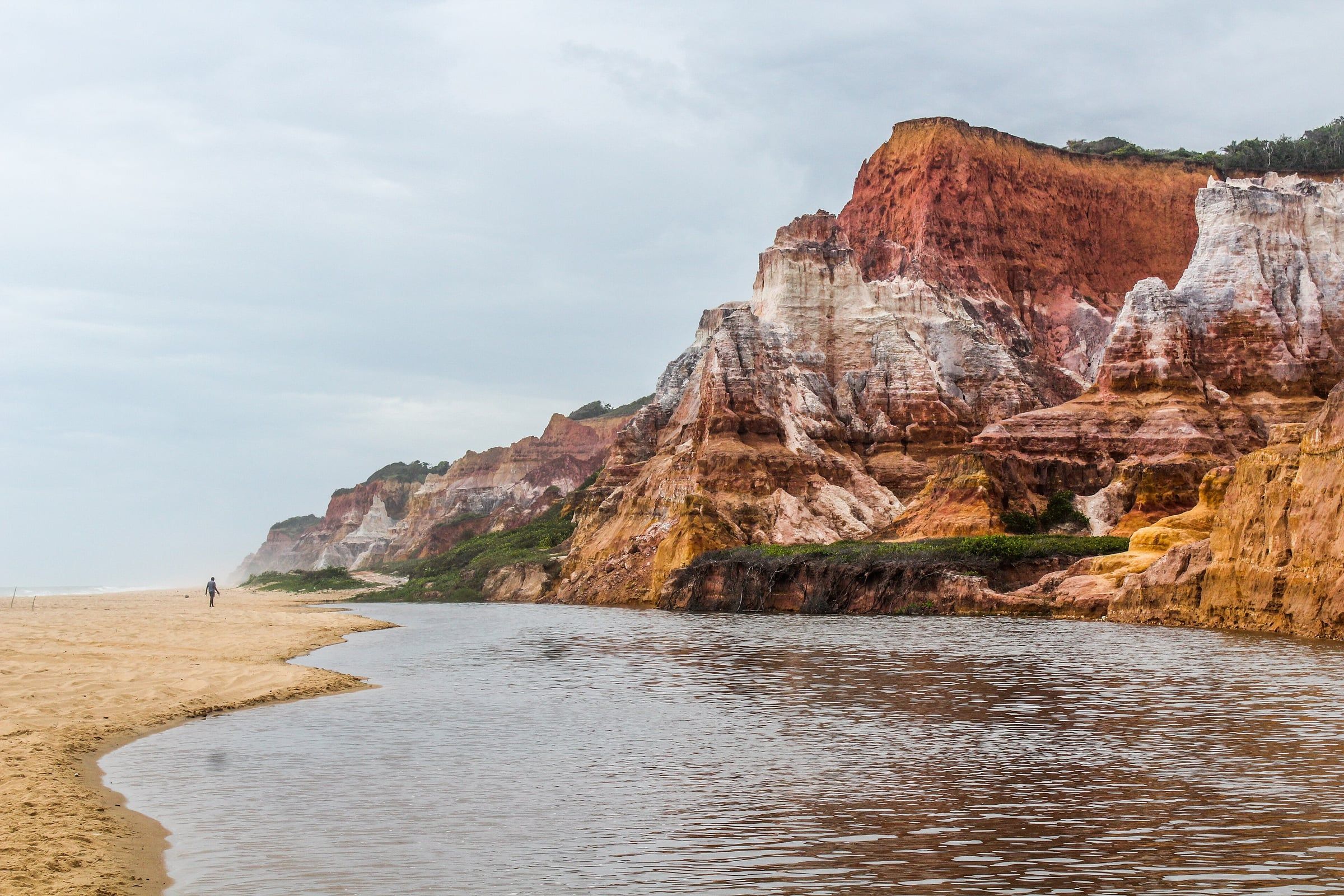 Falésias coloridas de vermelho, branco e ocre refletidas na água rasa da Praia do Gunga