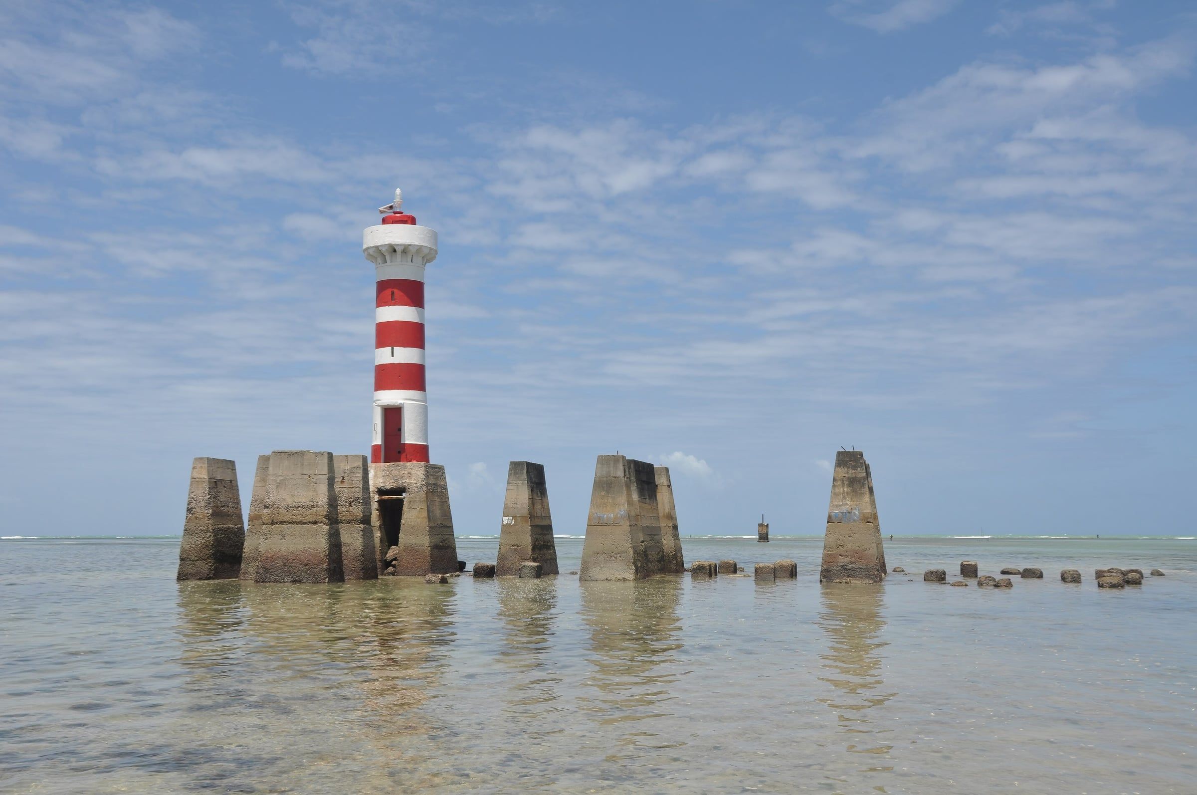 Farol listrado de vermelho e branco da Ponta Verde sobre pilares no mar raso e calmo