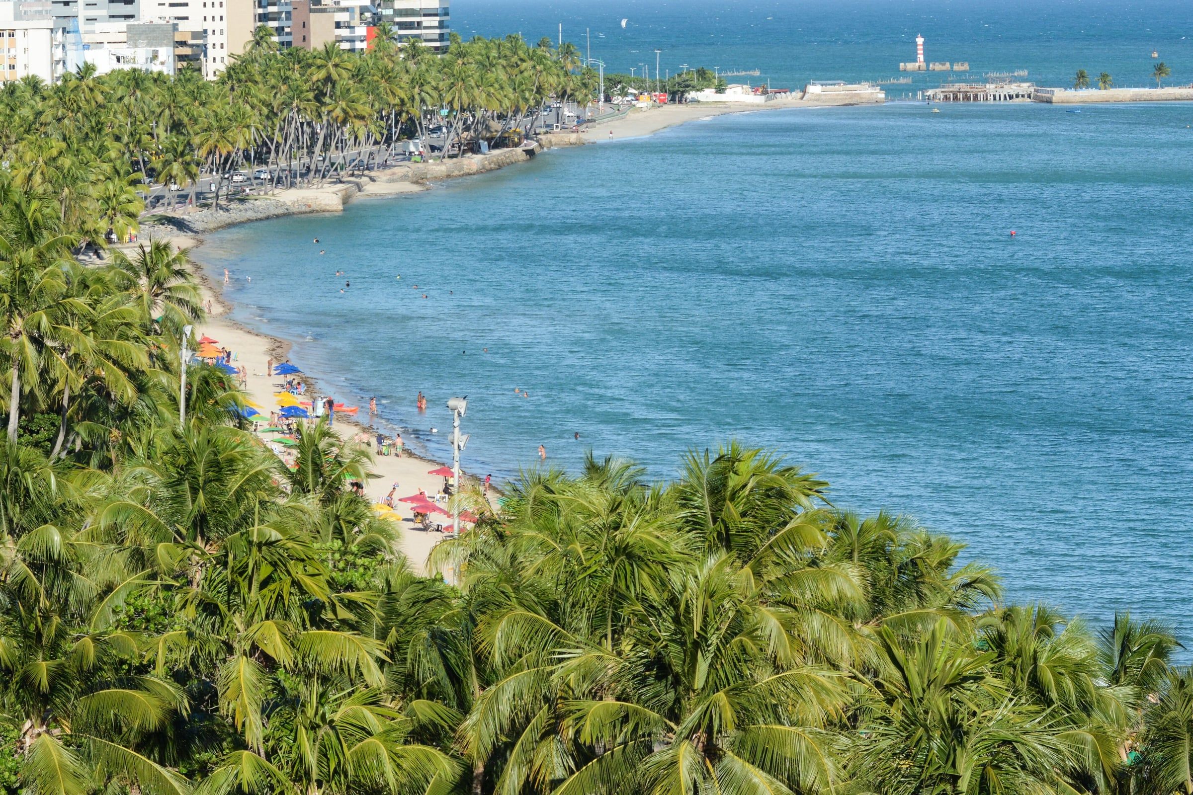 Orla da Pajuçara vista do alto, com coqueiros, faixa de areia e o mar verde e azul de Maceió