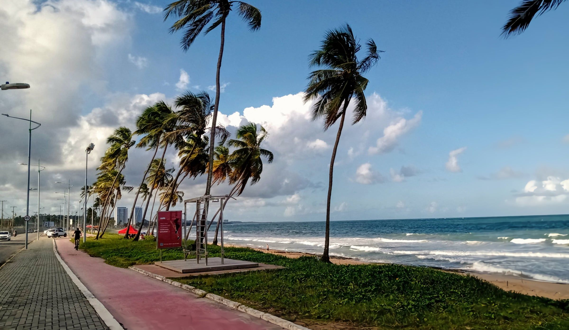 Calçadão com ciclovia e coqueiros à beira-mar na Praia de Cruz das Almas